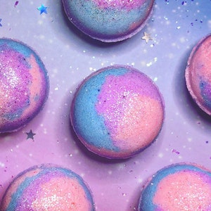 Puede incluir: Seis bombas de baño coloridas con temática de galaxia. Las bombas de baño son rosas, azules y moradas con purpurina.