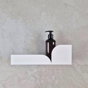 May include: A dark brown bottle with a black pump dispenser sits on a white, geometric shelf. The shelf is mounted on a light gray, textured wall. The design is minimalist and modern, suitable for bathroom or kitchen decor.