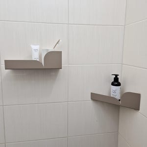 May include: Two corner shelves in a bathroom, one with a tube of body cream and a toothbrush, the other with a bottle of hand soap labeled "Almond"