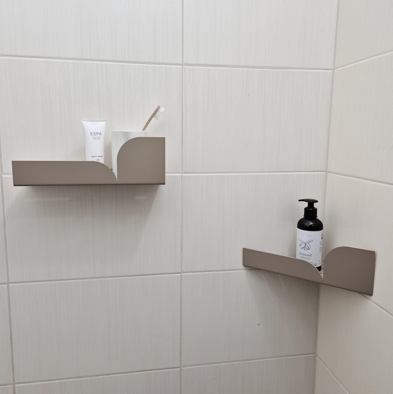 May include: Two corner shelves in a bathroom, one with a tube of body cream and a toothbrush, the other with a bottle of hand soap labeled "Almond"