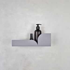 以下が含まれることがあります： 2 つの丸みを帯びた端を持つ灰色の金属製の棚。ポンプディスペンサー付きの濃い茶色のボトルと、スプレーノズル付きの小さな濃い茶色のボトルが棚の上に置かれています。