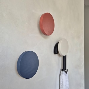 Op de afbeelding: Drie ronde wandhaken in terracotta, marineblauw en off-white. De off-white haak heeft een zwarte metalen arm die naar beneden wijst en een witte paraplu vasthoudt. Elke haak heeft een zichtbare houtnerfstructuur op het oppervlak.