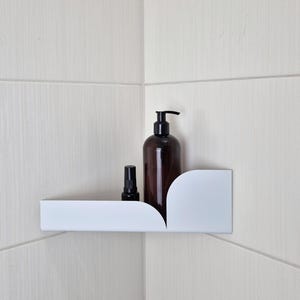 May include: White corner shelf with rounded edges, holding a brown bottle with a pump dispenser and a smaller brown spray bottle.