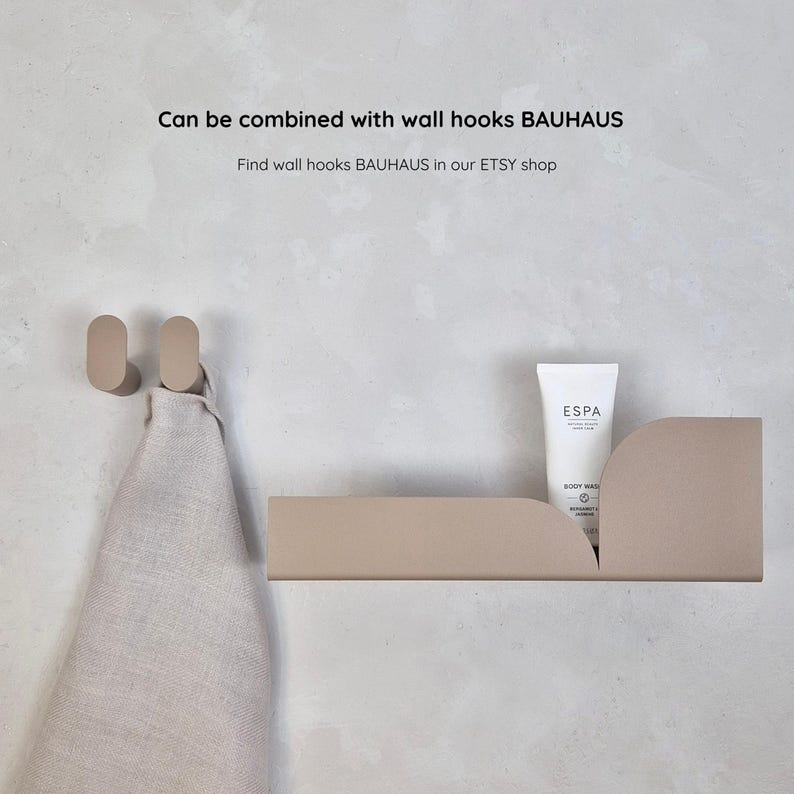 K&ouml;nnte beinhalten: Ein beiges Wandregal und zwei passende ovale Haken. Eine wei&szlig;e Tube ESPA Body Wash steht auf dem Regal. Ein beiges Handtuch h&auml;ngt an den Haken. Der Text auf dem Bild lautet "Can be combined with wall hooks BAUHAUS".