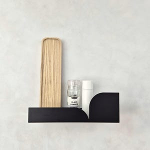 Könnte beinhalten: Schwarzes Metallregal mit abgerundeten Kanten, mit einem Holztablett, einem Glas-Gewürzstreuer mit der Aufschrift "Black & White" und einer weißen Flasche.