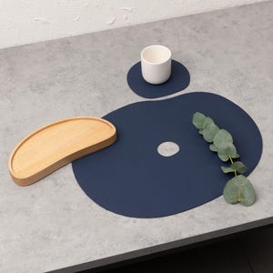 May include: A set of three blue leather placemats with a unique organic shape. The placemats have a hole in the center and are perfect for adding a touch of modern style to your dining table.