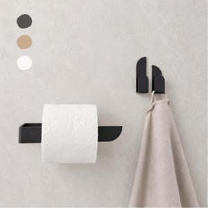 Könnte beinhalten: Ein Toilettenpapierhalter aus mattschwarzem Metall und zwei passende Wandhaken. Ein Haken hält ein beiges Handtuch. Drei kreisförmige Farbmuster in Dunkelgrau, Beige und Weiß sind oben links im Bild zur Referenz dargestellt.