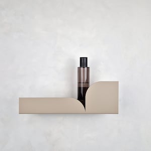 Può includere: Un ripiano a parete beige con un design curvo. Una bottiglia di vetro marrone con un tappo nero è appoggiata sullo scaffale.