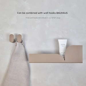 Beige shower shelf decorated with shower gel and 2 beige wall hooks decorated with linen towel