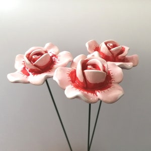 May include: Three pink ceramic roses with red centres on wire stems. The roses are arranged in a bouquet.