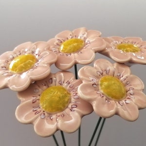 May include: Five pink ceramic flowers with yellow centers and a white outline. The flowers are on wire stems.