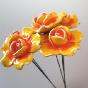 May include: Three yellow ceramic roses with orange centres on green stems. The roses are arranged in a bouquet.