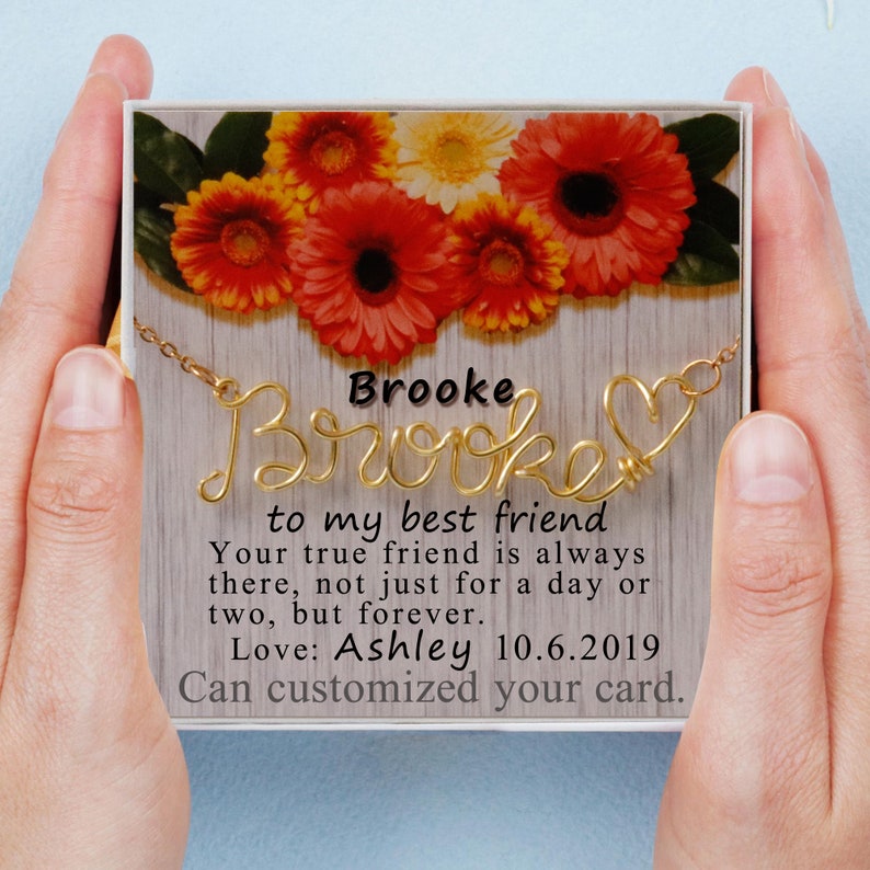 May include: A gold wire necklace with the name 'Brooke' spelled out in cursive with a heart at the end. The necklace is in a white gift box with a floral design on the lid. The text on the card reads: 'Brooke to my best friend Your true friend is always there, not just for a day or two, but forever. Love: Ashley 10.6.2019 Can customized your card.'