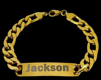 Puede incluir: Una pulsera de cadena dorada con una placa rectangular con el nombre. El nombre "Jackson" está grabado en la placa. La pulsera tiene un cierre de mosquetón y un diseño de eslabones de cadena gruesos.