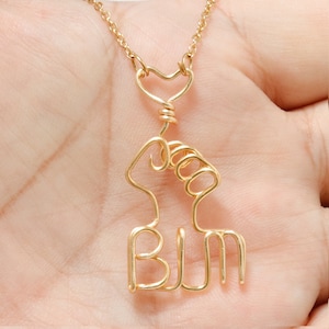 May include: Gold necklace with a heart and a raised fist with the letters BLM.