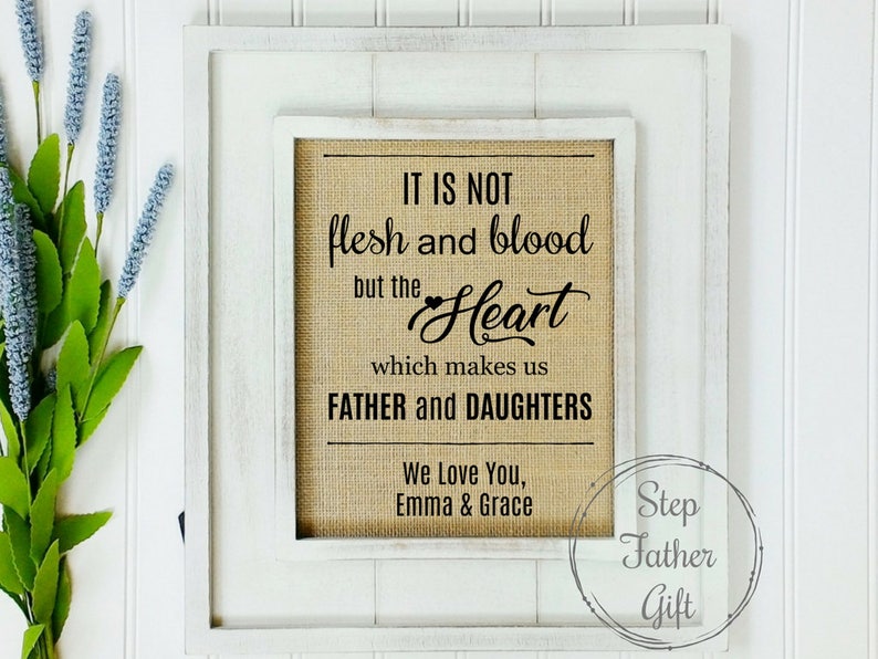 May include: White framed burlap sign with black text that reads "It is not flesh and blood but the Heart which makes us Father and Daughters. We Love You, Emma & Grace." The bottom right corner of the sign has a circle with the text "Step Father Gift".