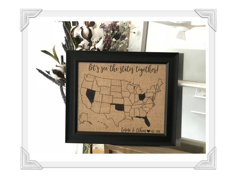 May include: A black framed burlap map of the United States with the text "Let's see the states together!" and "Emily & Ethan" with a heart and the year 2018.