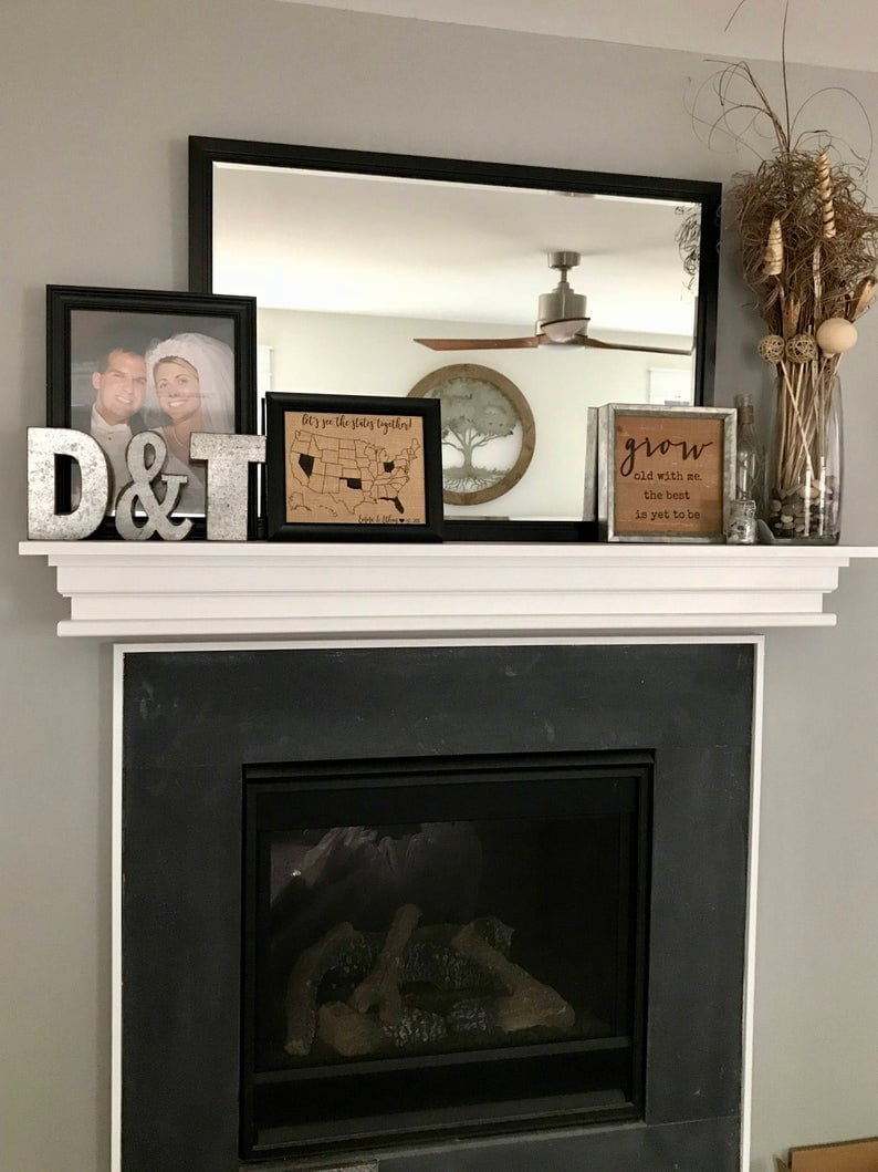 May include: A white mantelpiece with a black fireplace below. The mantelpiece is decorated with a framed photo, a framed map of the United States, a wooden sign that says "grow old with me, the best is yet to be", and a metal sign that says "D&T".