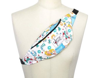 May include: White fanny pack with a black zipper and strap, featuring a colorful Alice in Wonderland print. The design includes Alice, the White Rabbit, and floral elements. The bag is displayed on a mannequin.