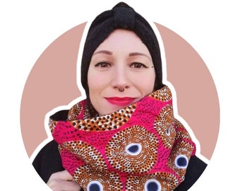 May include: A vibrant pink and brown patterned cowl scarf. The scarf features a repeating circular design with blue and white accents. The person in the image is wearing a black head covering and a black top.