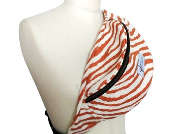 May include: A fanny pack with a zebra stripe pattern in orange and white, displayed on a mannequin. The bag has a black zipper and strap. A small tag with text is visible on the side.