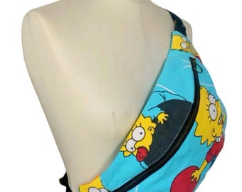 May include: A light blue fanny pack featuring a repeating cartoon character design. The pack has a black zipper and strap, and is displayed on a mannequin. The bag is a fun, colorful accessory.
