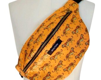 May include: Orange fanny pack with a repeating tiger pattern. The bag has a black zipper and a black strap. A small black label reads "Jenny Patsy". The bag is displayed on a mannequin.