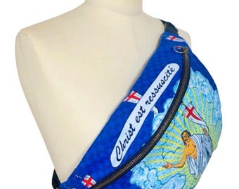 May include: Blue fanny pack with a zipper closure and a graphic of Jesus Christ rising, with the text "Christ est ressuscité". The bag has a blue wave pattern and a black strap.