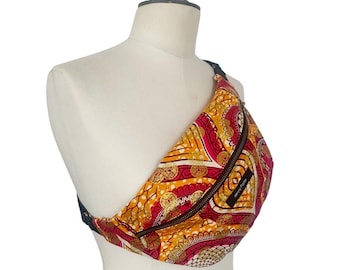 May include: A colorful fanny pack with a vibrant pattern of red, yellow, and white geometric shapes. The bag has a black zipper and strap, and the text "Jenny Folty" is visible on a small black tag.