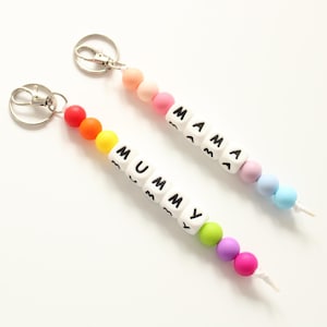 May include: Two rainbow coloured beaded keychains with the words "MUMMY" and "MAMA" spelled out on white beads.