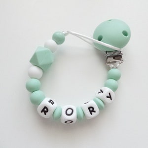 May include: A mint green silicone baby teether with a white clip and beads. The teether has the name "Rory" spelled out in black letters on white beads.