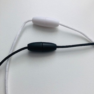 May include: A white cord with a white plastic toggle and a black cord with a black plastic toggle.