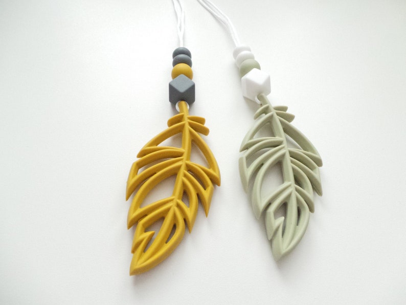 May include: Two silicone necklaces with feather charms. One necklace has a yellow feather charm with gray and yellow beads. The other necklace has a green feather charm with white and gray beads.