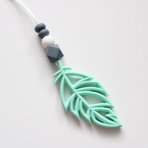 May include: A mint green silicone feather pendant with a white and gray silicone bead necklace.