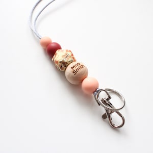 May include: A light pink, red, and brown beaded lanyard with a wooden bead that says "Miss Smith" and a silver swivel clasp.