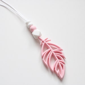 May include: A pink silicone baby teether with a feather shape and white silicone beads on a white cord.