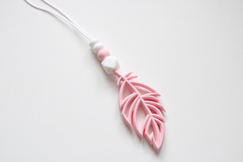 May include: A pink silicone baby teether with a feather shape and white silicone beads on a white cord.