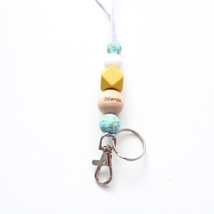 May include: A blue, white, and yellow beaded lanyard with a wooden bead that says "Jolanda" and a silver key chain.