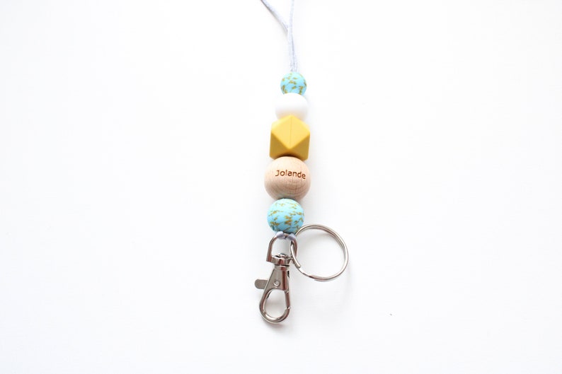 May include: A blue, white, and yellow beaded lanyard with a wooden bead that says "Jolanda" and a silver key chain.