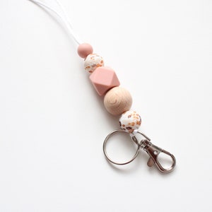 May include: A pink and brown beaded lanyard with a silver key chain. The lanyard has a white cord and features a variety of round and geometric beads.