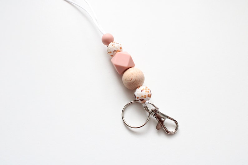 May include: A pink and brown beaded lanyard with a silver key chain. The lanyard has a white cord and features a variety of round and geometric beads.