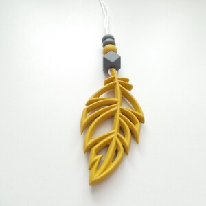 May include: A yellow silicone feather pendant with a gray silicone bead and a gray diamond-shaped silicone bead on a white string.