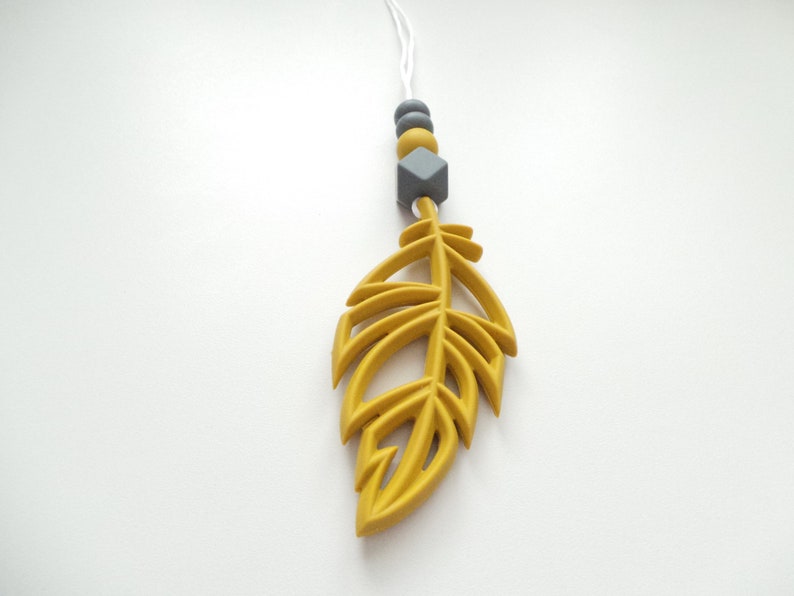 May include: A yellow silicone feather pendant with a gray silicone bead and a gray diamond-shaped silicone bead on a white string.