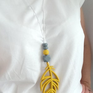 May include: A yellow silicone feather pendant necklace with gray and yellow silicone beads. The necklace is on a white cord.