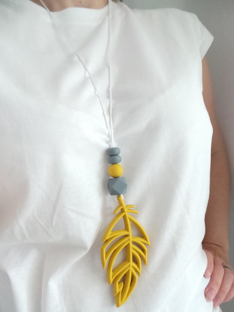 May include: A yellow silicone feather pendant necklace with gray and yellow silicone beads. The necklace is on a white cord.