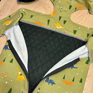May include: A green sleeping bag with a zipper down the front. The sleeping bag has a black quilted lining and a pattern of dinosaurs, trees, stars, and moons.