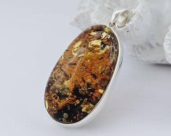 May include: A silver pendant with a large oval amber stone. The amber is a mix of brown, yellow, and black.
