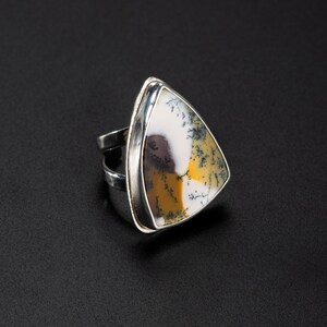 Puede incluir: Un anillo de plata con una piedra triangular grande. La piedra presenta un patr&oacute;n &uacute;nico de blanco, amarillo y negro, engastada en una banda de plata pulida. El anillo es una pieza llamativa.