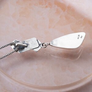 May include: Silver necklace with a teardrop pendant and a rectangular charm. The pendant has the text "925" and "MILSS" engraved on the back.