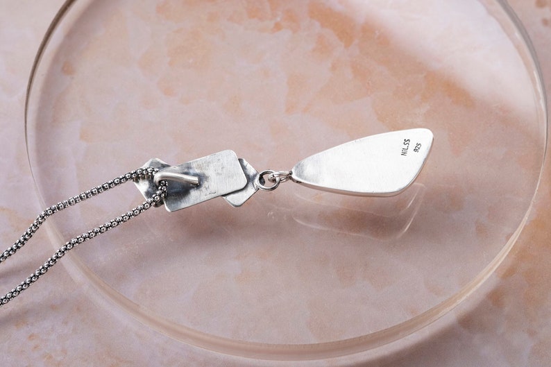 May include: Silver necklace with a teardrop pendant and a rectangular charm. The pendant has the text "925" and "MILSS" engraved on the back.